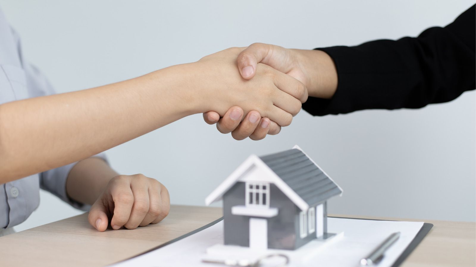 two people shaking hands in front of a model house - mortgage broker gold coast