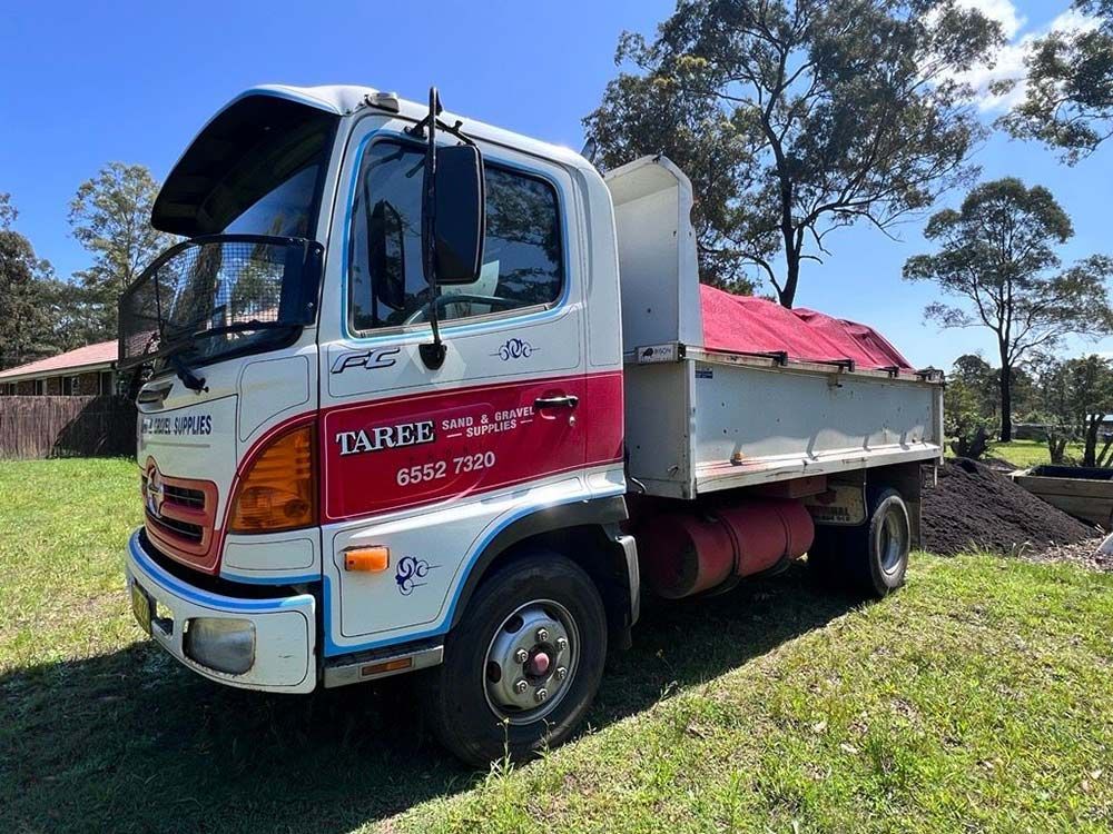 A White and Red Dump Truck is Parked in a Grassy Field — HKL Landscape Supplies in Gloucester, NSW