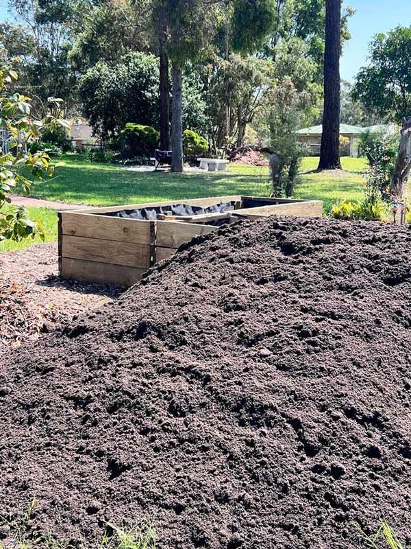 A Pile of Dirt is Sitting in a Yard Next to a Wooden Box — HKL Landscape Supplies in Forster, NSW 