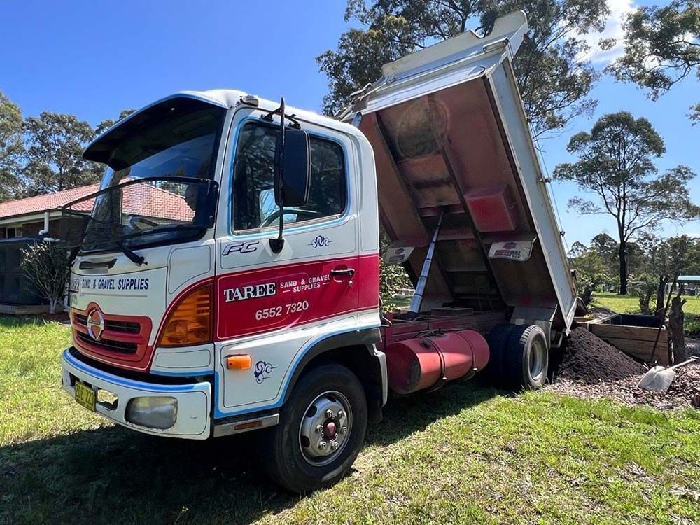 A White and Red Dump Truck is Parked in a Grassy Field — HKL Landscape Supplies in Gloucester, NSW