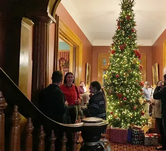 Festive living room with a decorated Christmas tree and people mingling in warm lighting
