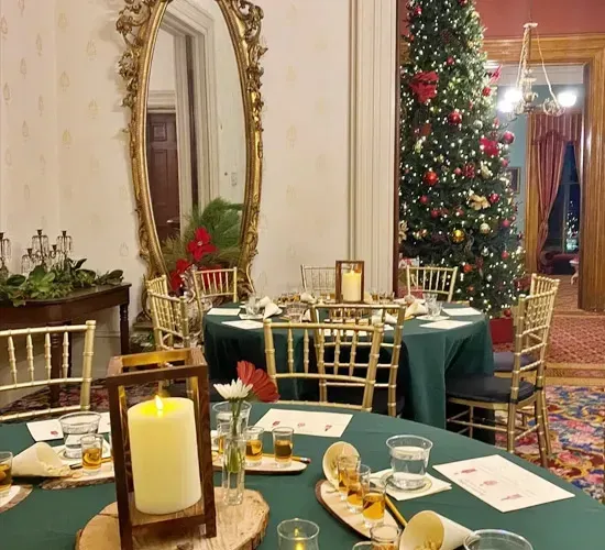 Elegant holiday dining room with decorated Christmas tree, gold chairs, and candlelit tables