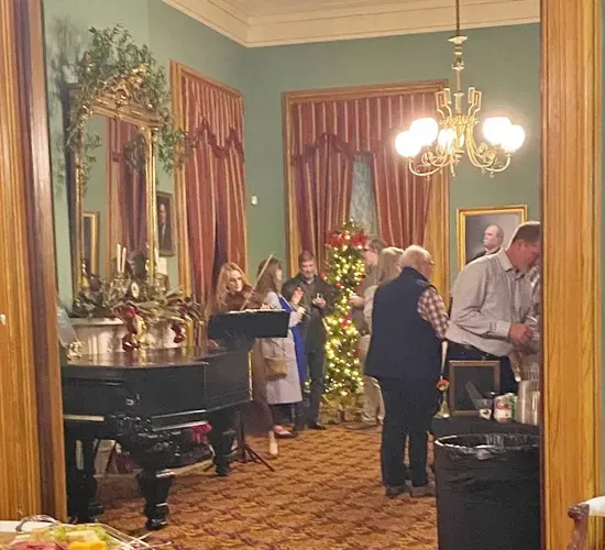 Guests mingling in an elegant room with chandeliers, tall windows, and ornate decor
