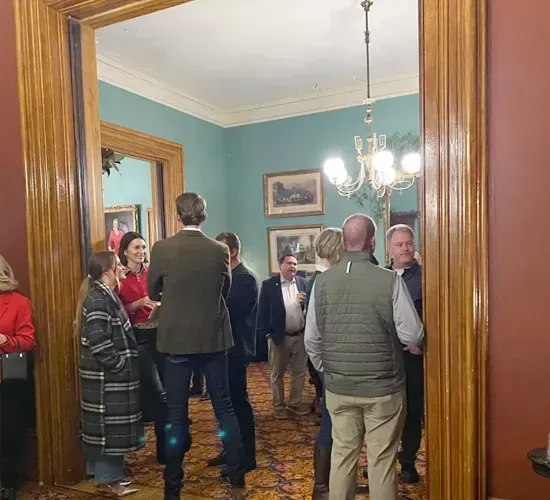 People gathered in a blue-walled room, standing and talking at a formal indoor event.