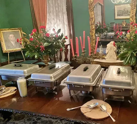 Buffet table with silver chafing dishes, flowers, candles, and framed portraits in a formal room