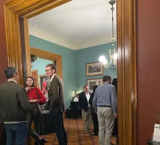 People socializing in a teal-walled room with a wooden doorway and chandelier.
