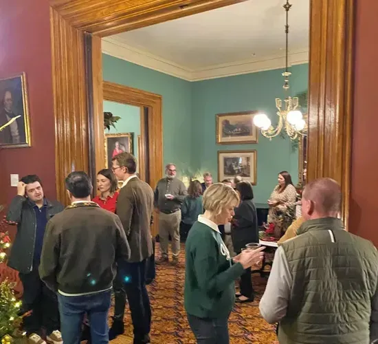 People mingling in a formal room with teal walls, wood trim, and a chandelier.