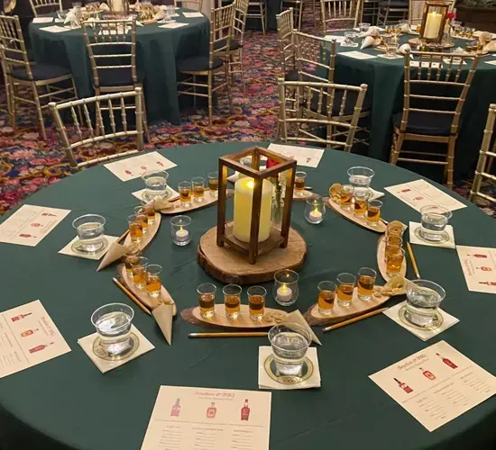 Round banquet table set with green cloth, lantern centerpiece, candles, glasses, and appetizers in a ballroom