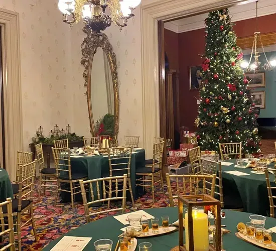 Elegant holiday dining room with decorated Christmas tree, gold chairs, and green table settings