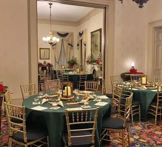 Elegant dining room with round tables, green tablecloths, gold chairs, and floral carpet