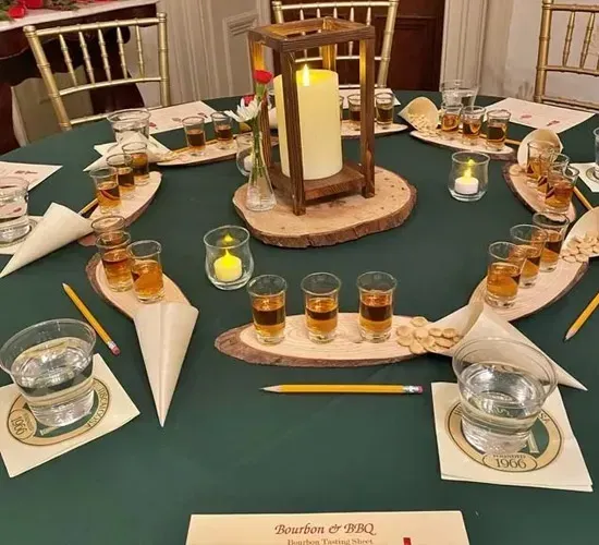 Round banquet table set for a candlelit event, with glasses, rolled napkins, and green tablecloth.