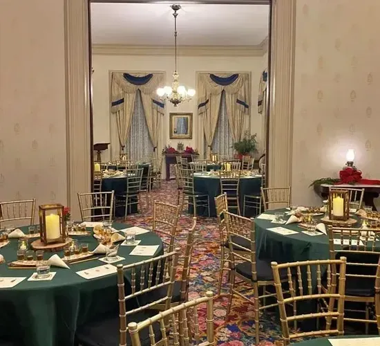 Elegant banquet room with round tables, green tablecloths, gold chairs, and patterned carpet under chandeliers