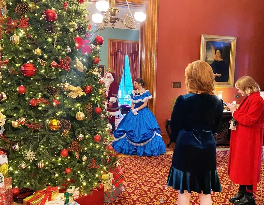 Christmas tree in a decorated room while a woman in a blue gown performs for guests