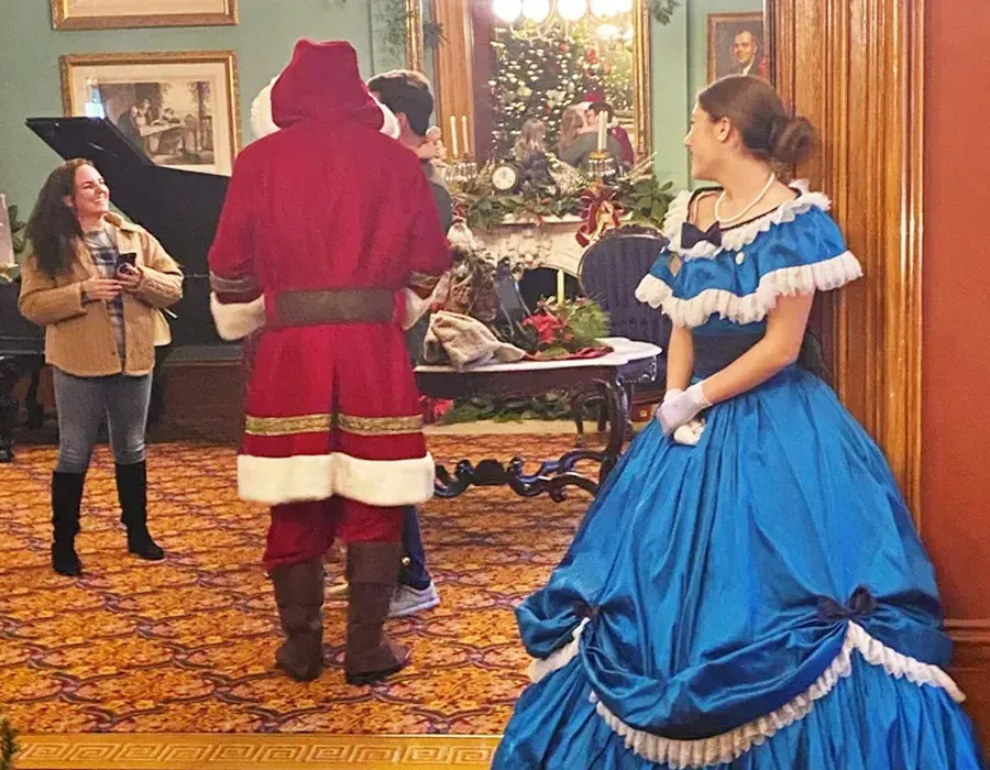 Costumed people posing in a decorated holiday room with a Christmas tree and ornate fireplace