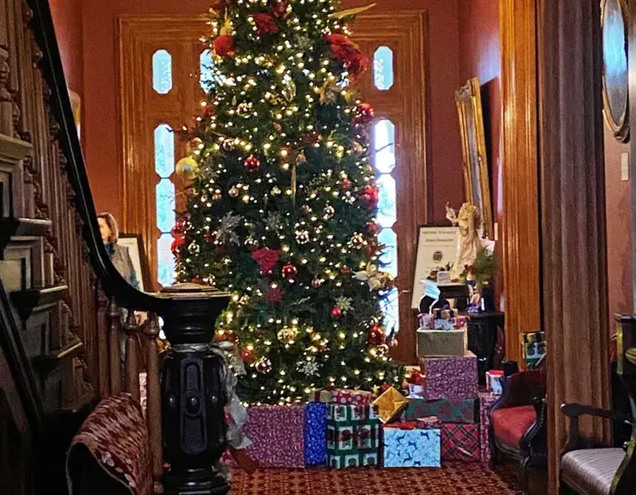 Decorated Christmas tree with presents in a warmly lit wooden hallway