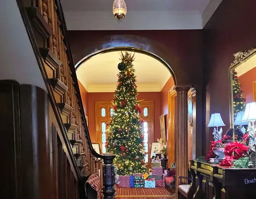 Cozy home hallway with a decorated Christmas tree, wood staircase, and festive lights
