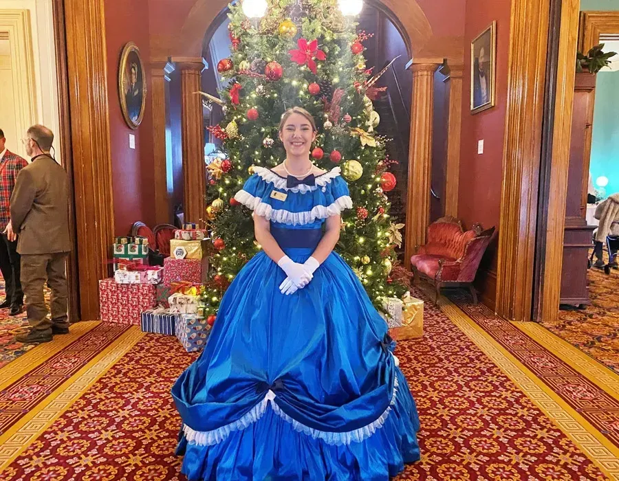 Decorated Christmas tree beside two costumed figures in a festive, warmly lit room
