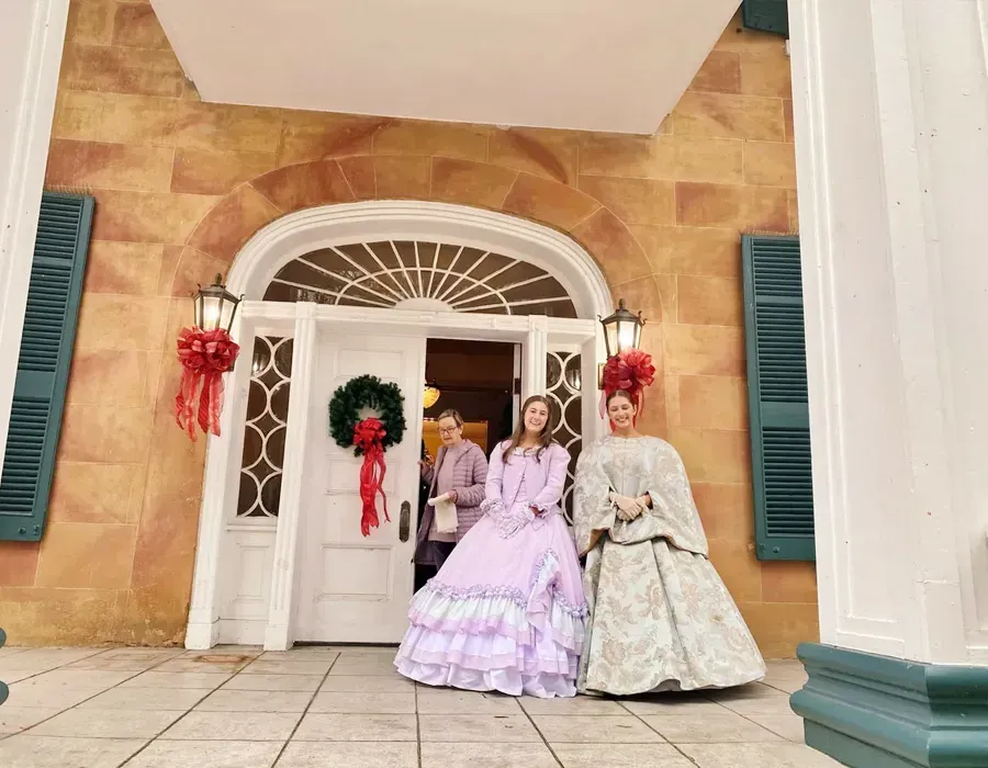 Three people in pastel dresses pose in front of a decorated arched doorway.