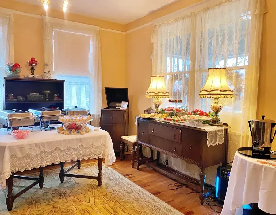 Elegant dining room with buffet table, lace-covered table, lamps, and large windows