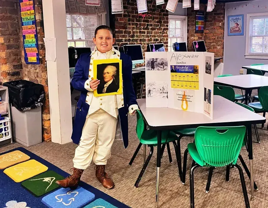 Student standing in a classroom holding a framed portrait beside a presentation board.