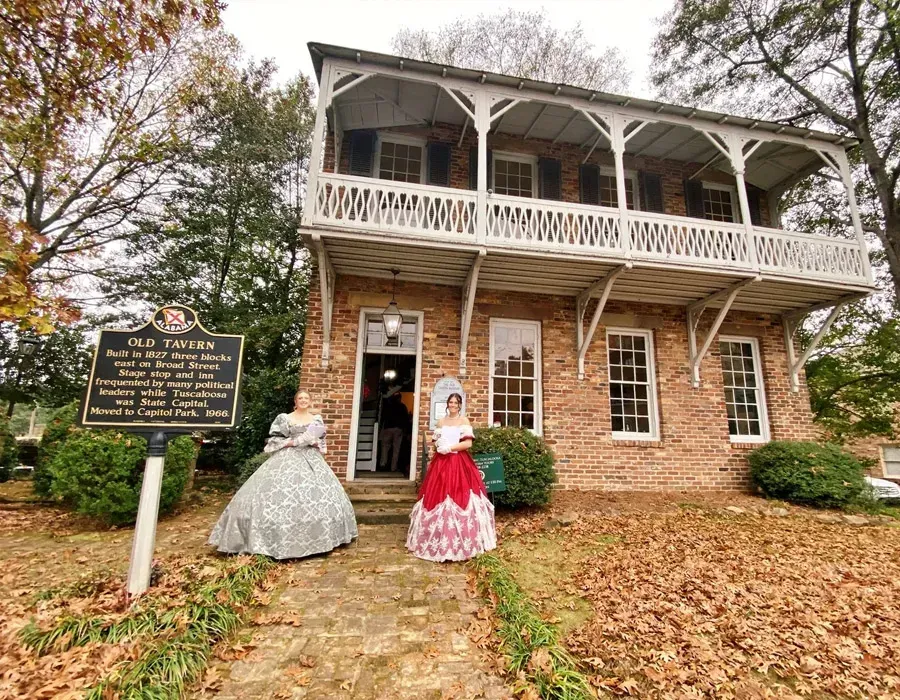 Historic brick house with two mannequins in period dresses on a leaf-covered path