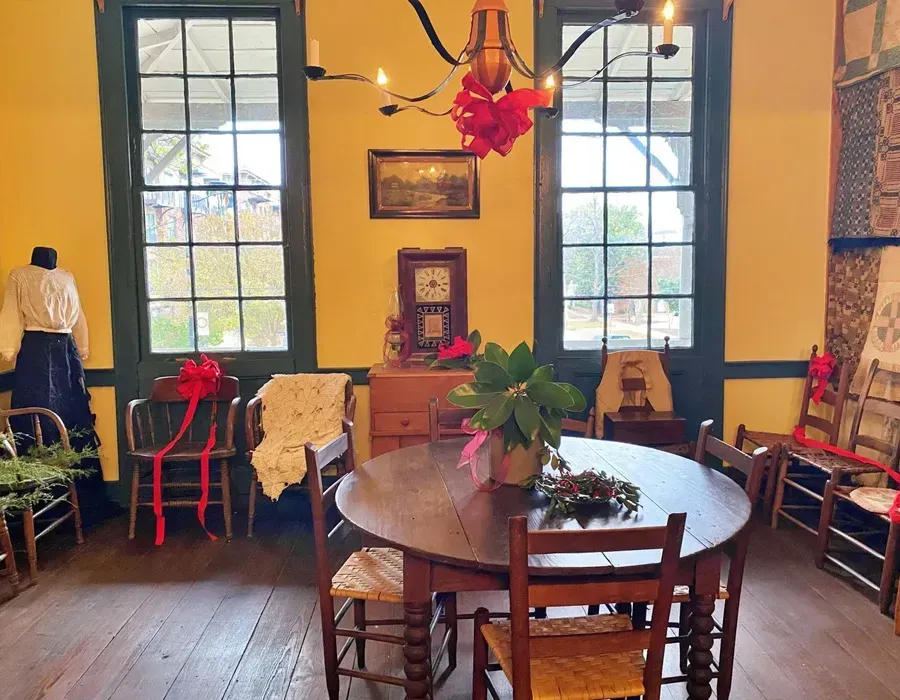Cozy dining room with round wooden table, chairs, large windows, plants, and warm lighting