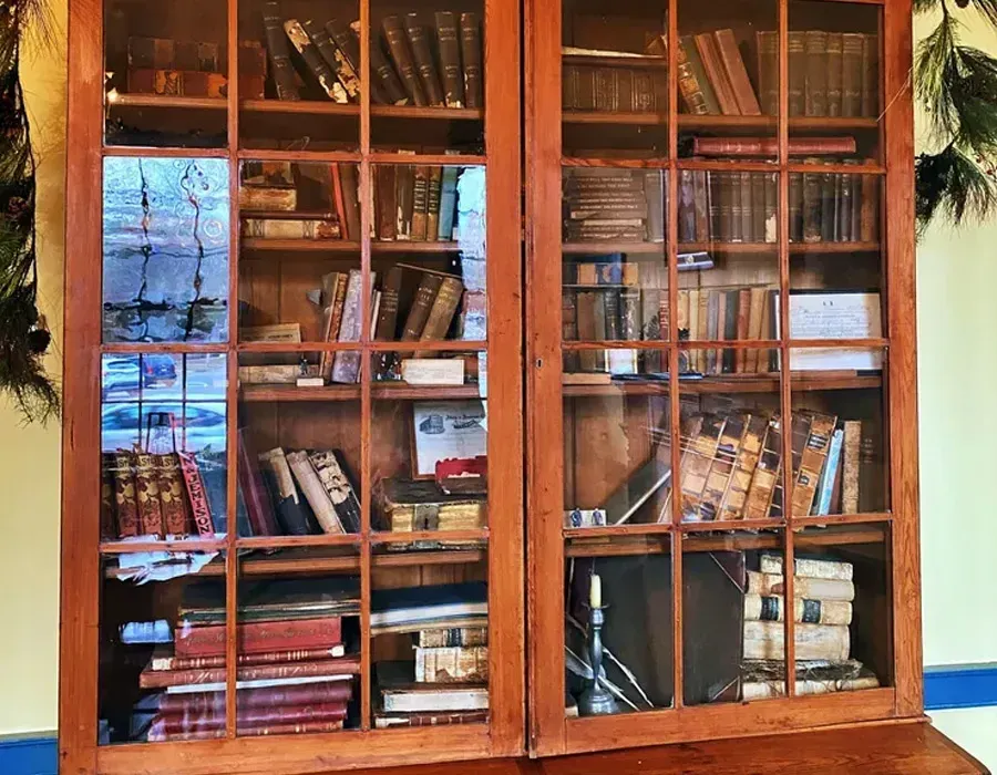 Wooden glass-front bookcase filled with books and decor, with a window reflection in the background.