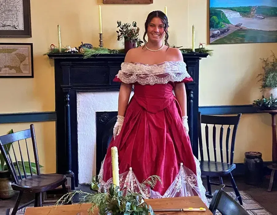 Person in a red off-the-shoulder gown standing in a room with a fireplace and dining table