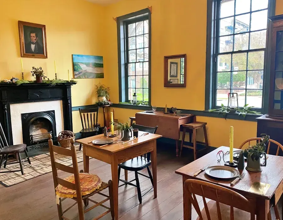 Cozy yellow café interior with wooden tables, large windows, black fireplace, and a few potted plants