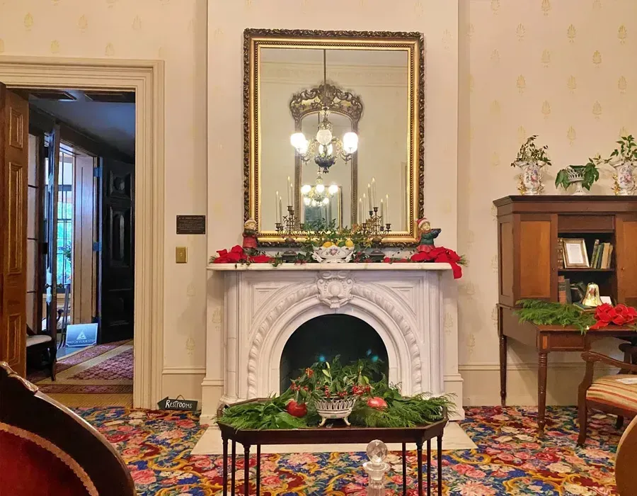Elegant room with white fireplace, ornate mirror, floral decor, and colorful patterned carpet