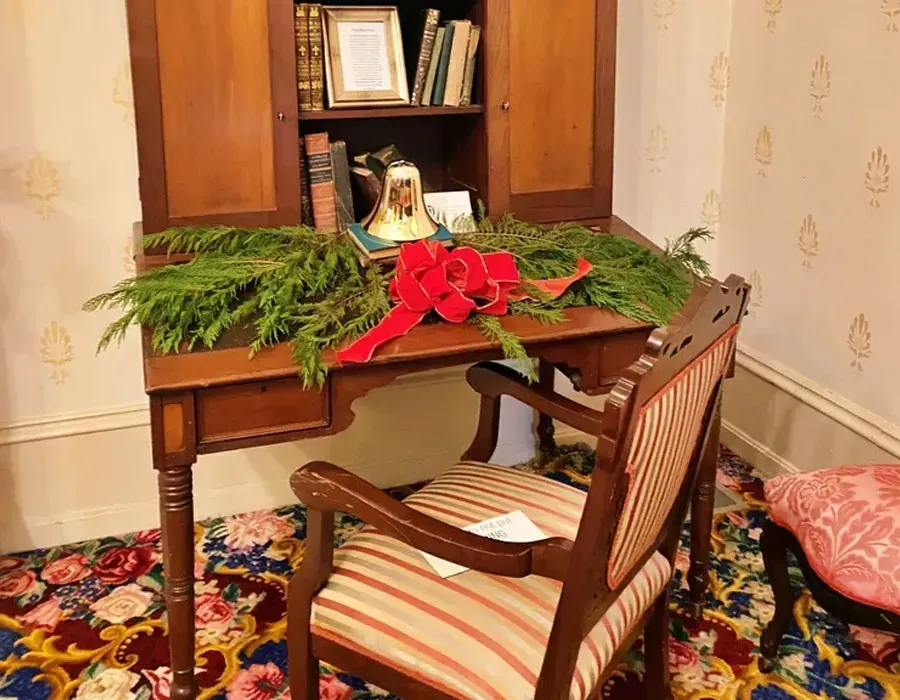 Decorated wooden desk with red bow, greenery, and a chair in a cozy room