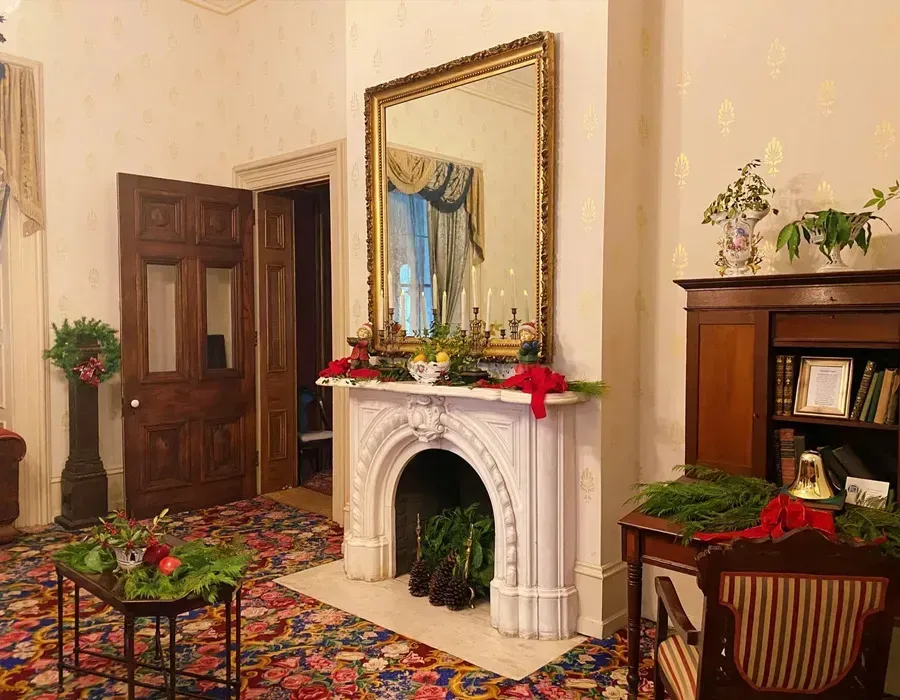 Elegant living room with ornate white fireplace, large mirror, floral rug, and dark wooden furniture