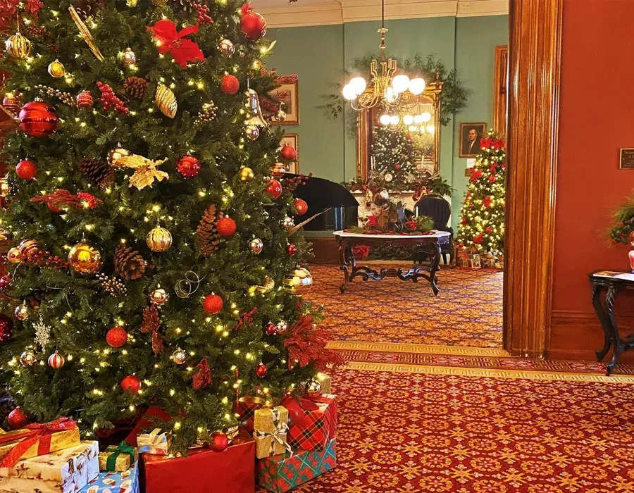 Decorated Christmas trees and gifts in a warmly lit hotel lobby with red carpet and festive decor