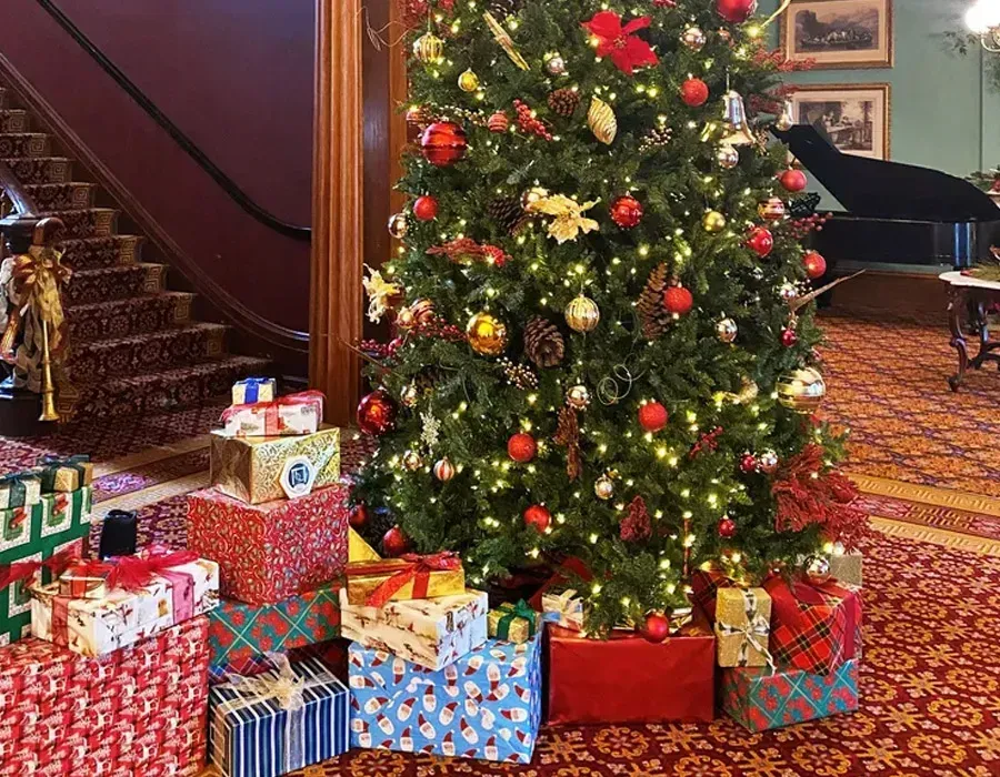 Decorated Christmas tree with wrapped gifts in a warmly lit room near a staircase