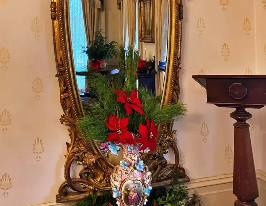 Decorative mirror with gold frame, red poinsettias, and greenery beside a wooden pedestal table
