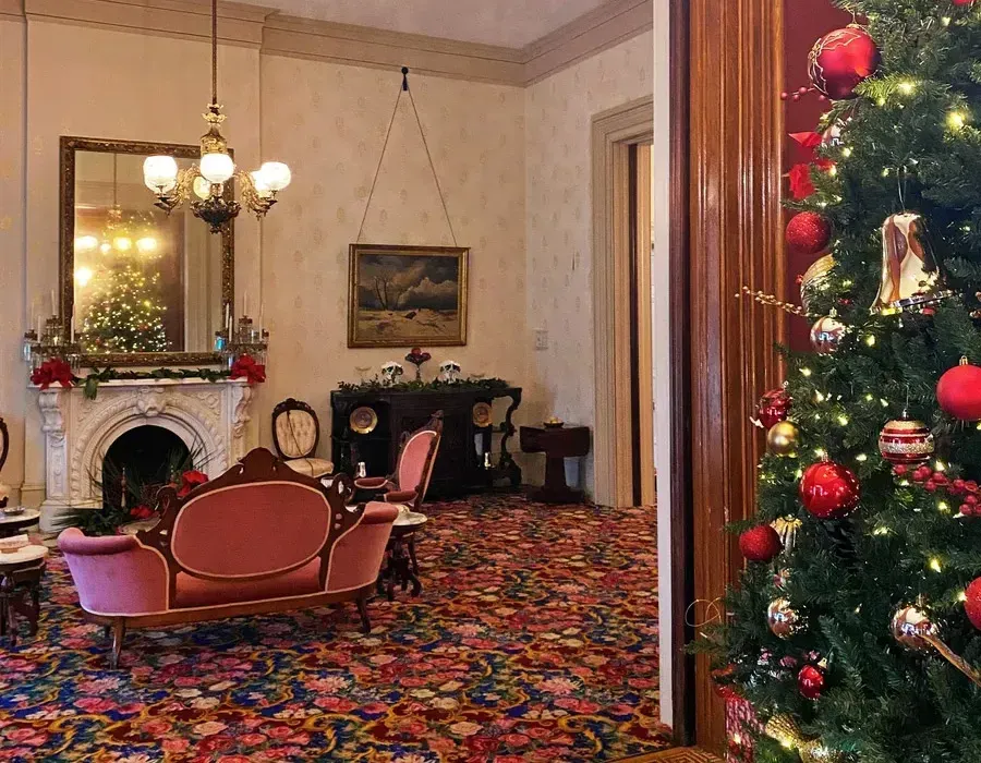 Festive living room with a decorated Christmas tree, pink sofa, fireplace, and patterned carpet