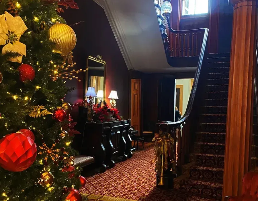 Festive hallway with a decorated Christmas tree, red accents, and a staircase in a warmly lit home
