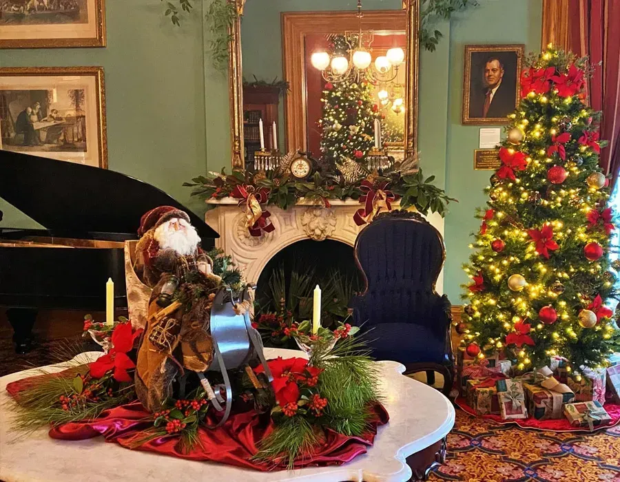 Festive living room with decorated Christmas tree, fireplace, piano, and holiday table centerpiece
