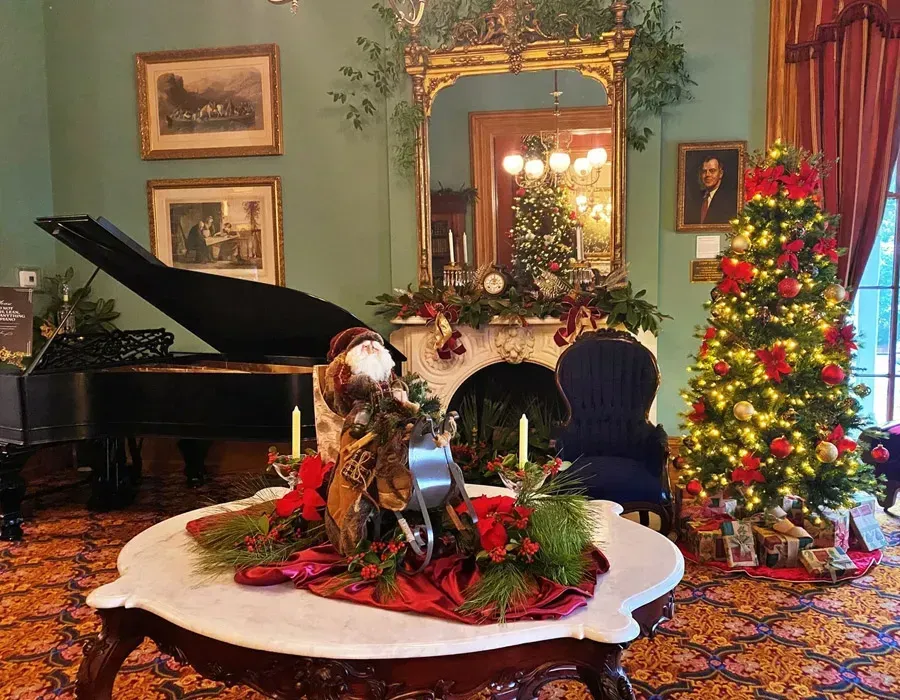 Elegant living room with Christmas tree, grand piano, fireplace, and holiday floral centerpiece