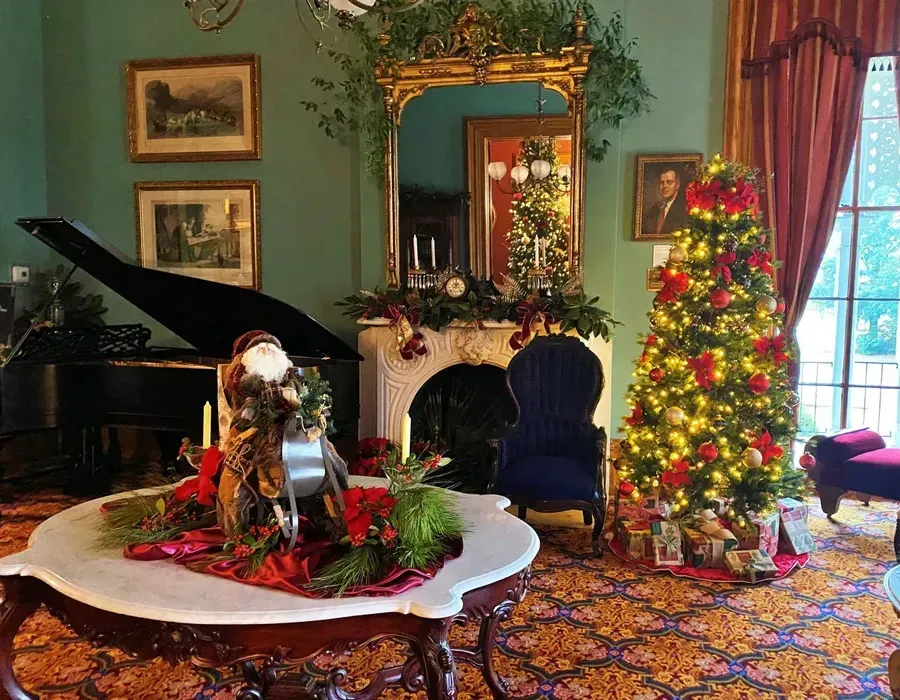 Elegant parlor with grand piano, Christmas tree, and festive red-and-gold holiday decor