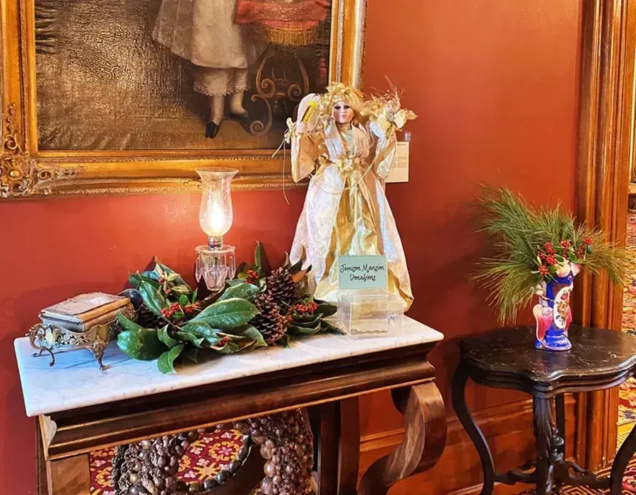 Decorated console table with angel figurine, flowers, lamp, and framed art in a warm orange room
