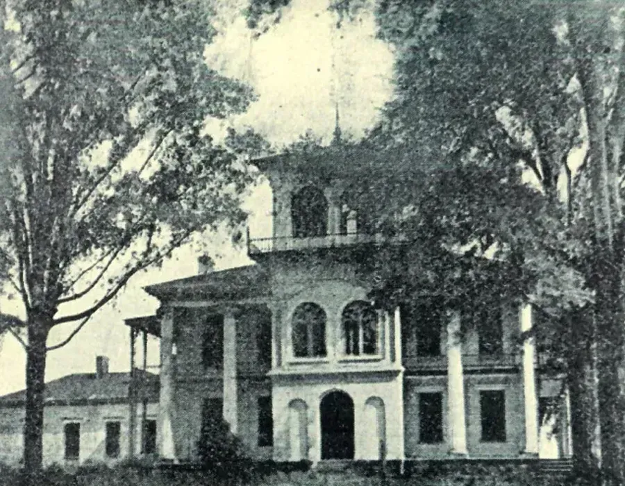 Historic two-story house with cupola, arched windows, and trees in front