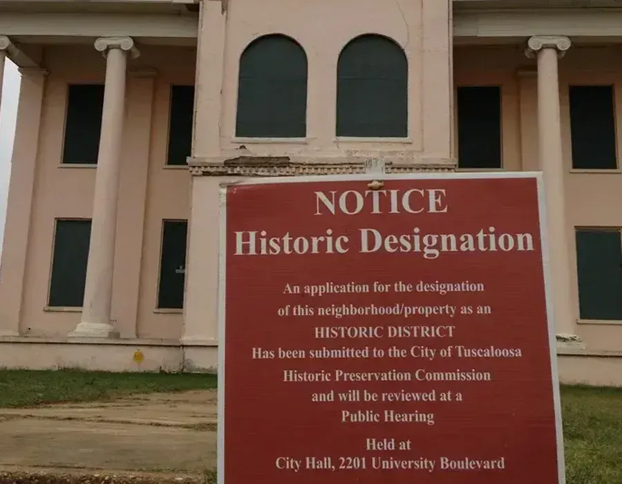 Red notice sign for historic designation in front of a beige building with columns.