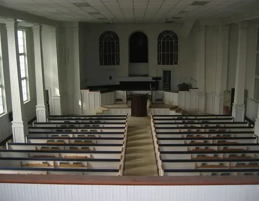 Empty church sanctuary with white pews facing a central pulpit and stained-glass windows.