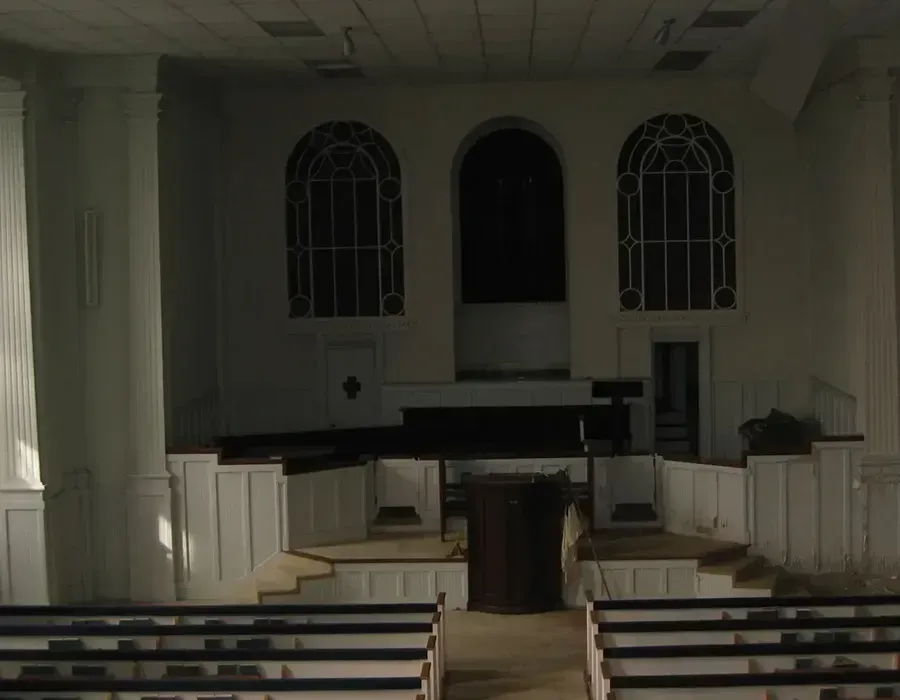 Empty church sanctuary with pews, altar, and arched windows in dim light