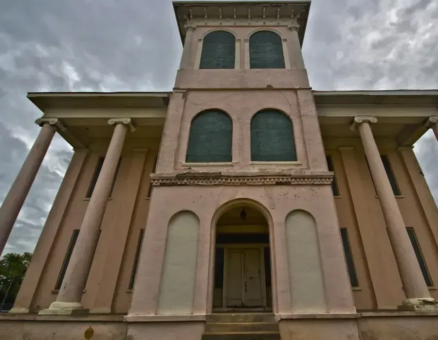 Historic beige building with tall columns and arched windows under a cloudy sky