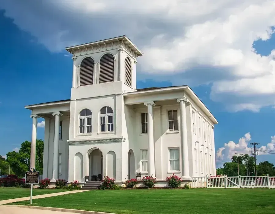 White church with a tall bell tower on a green lawn under a blue sky with clouds