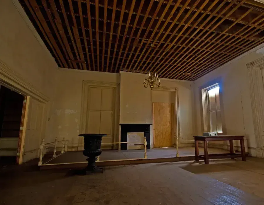 Abandoned room with bare wooden ceiling, fireplace, doors, and a bench lit by daylight from windows