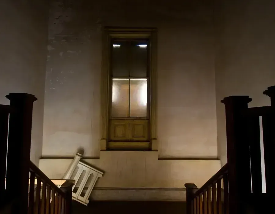 Dim stairwell with a lit window and a tipped chair against the wall.
