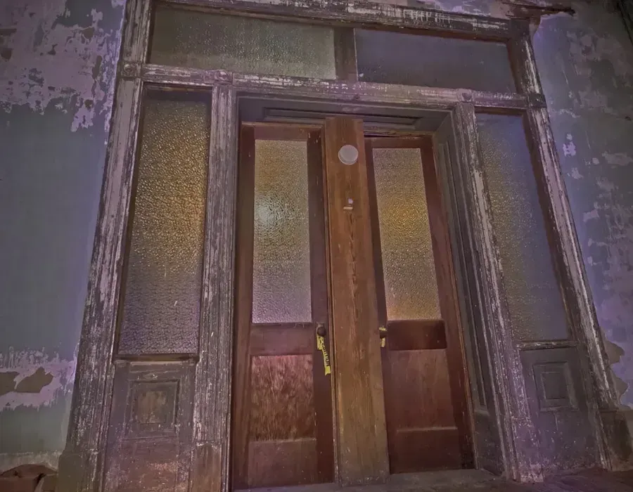 Old wooden double door with frosted glass panels in a worn, peeling wall